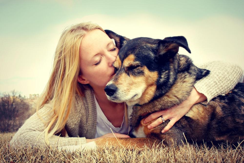 Female owner laying down in dry grass with arms around her older dog