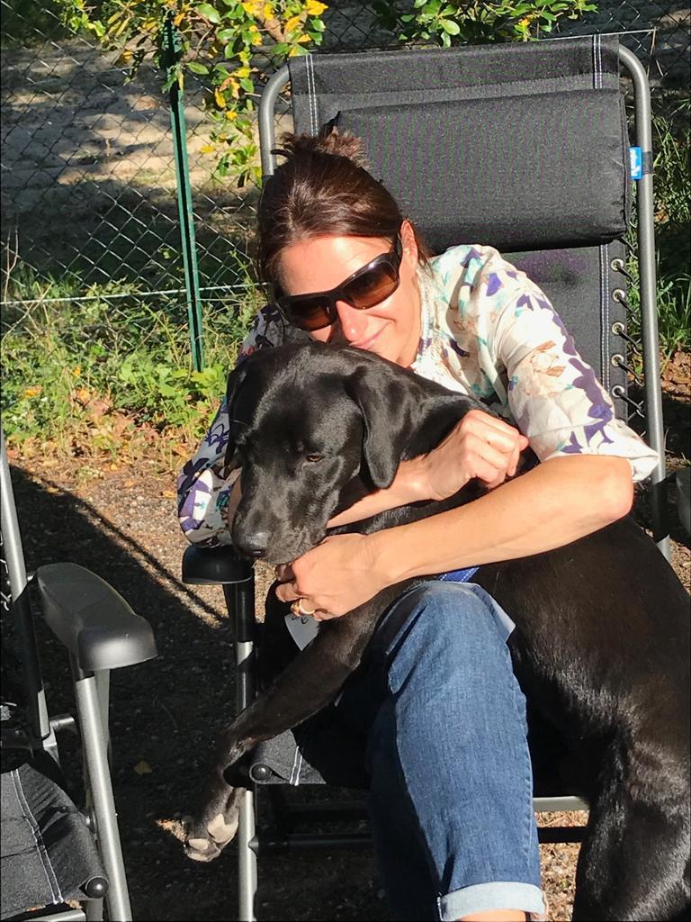 Jago black labrador and being hugged by his owner as she sits on a camping chair